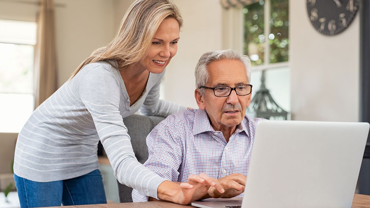 woman helps senior citizen man use a laptop