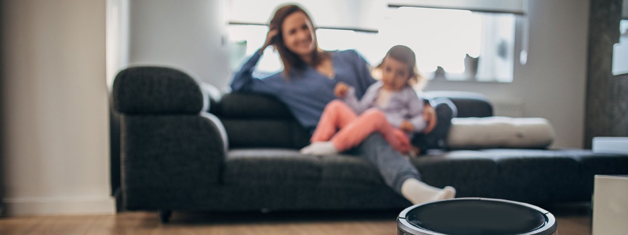 mom and daughter relax on couch while robot vacuum cleans the floor
