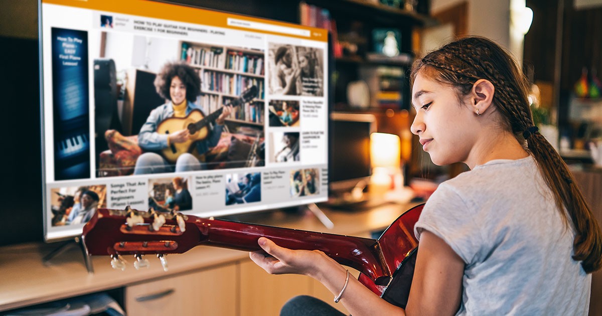Um jovem adolescente faz uma aula de guitarra virtual em uma TV inteligente