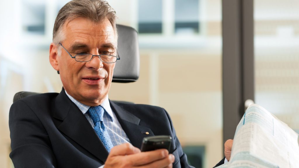 A older male executive checks his email on his phone. 
