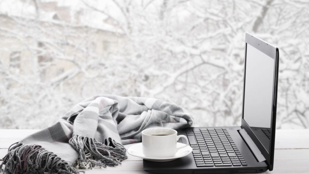 A laptop in front of a window on a cold and snowy day. 